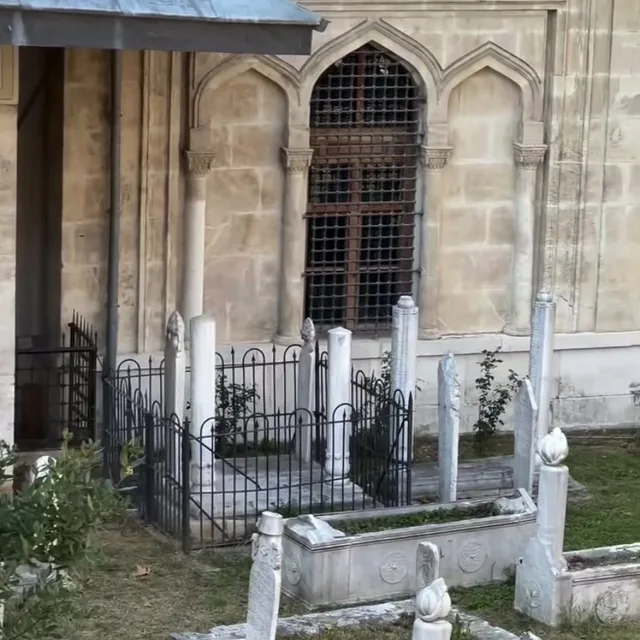 Yan taraftaki tarihi medresenin taş cephesi, parmaklıklı penceresi ve avlusu